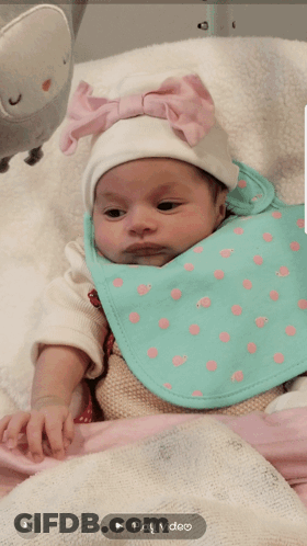 A Baby Wearing A Bib And A White Hat With A Play Video Button Below It GIF
