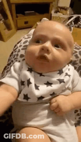A Baby Wearing A Bib Is Being Held By A Person And Making A Funny Face . GIF