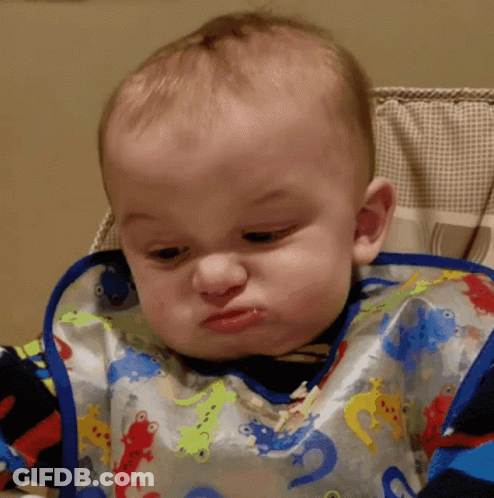 A Baby Wearing A Bib With Lizards On It Making A Funny Face GIF