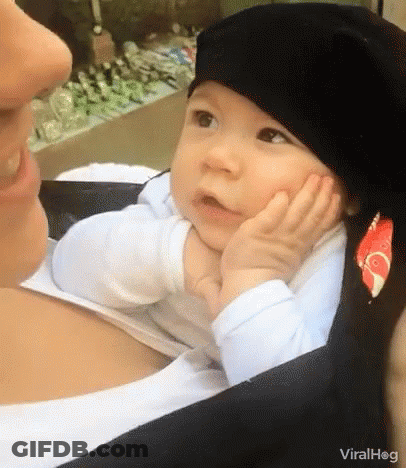 A Baby Wearing A Black Hat Is Sitting On A Woman 'S Lap . GIF