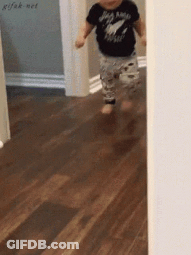 A Baby Wearing A Black Shirt That Says Rock N Roll Is Running On A Wood Floor GIF