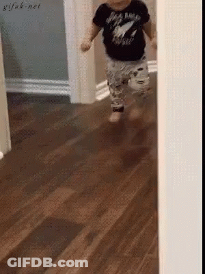 A Baby Wearing A Black Shirt That Says Rock N Roll Is Running On A Wooden Floor GIF
