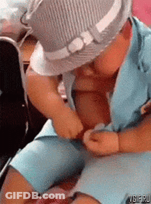 A Baby Wearing A Hat Is Sitting On A Woman 'S Lap And Playing With Her Clothes . GIF