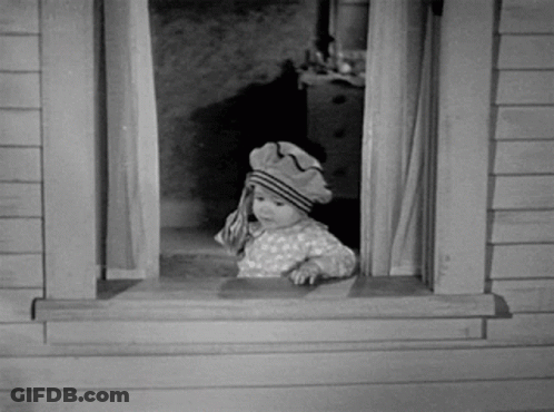 A Baby Wearing A Hat Looks Out A Window GIF