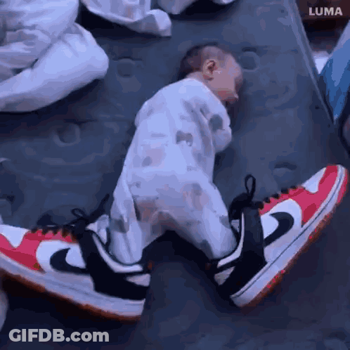 A Baby Wearing A Pair Of Nike Shoes Is Sleeping On A Bed . GIF
