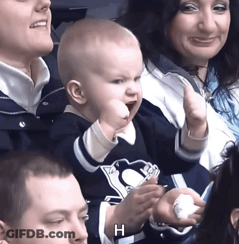 A Baby Wearing A Penguins Jersey Holds Up His Fist In The Air GIF
