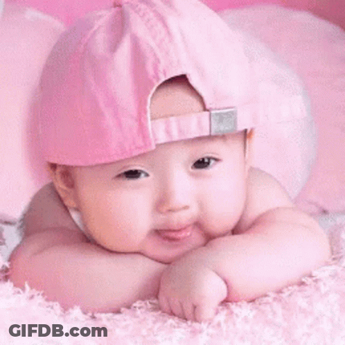 A Baby Wearing A Pink Hat Is Laying Down On A Pink Blanket GIF