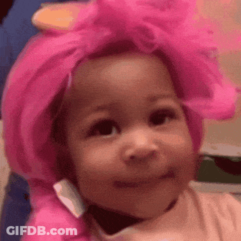 A Baby Wearing A Pink Wig And A Pink Hat Is Smiling . GIF