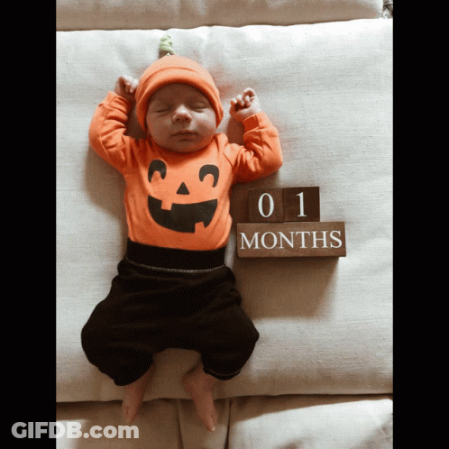 A Baby Wearing A Pumpkin Outfit Is Sleeping Next To A Sign That Says 1 Months GIF