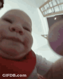 A Baby Wearing A Red Bib Is Looking At The Camera And Smiling . GIF