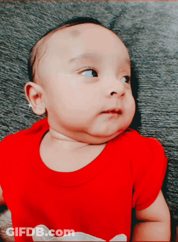 A Baby Wearing A Red Shirt With A Mouse On It Looks At The Camera GIF