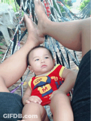 A Baby Wearing A Shirt That Says Love On It Sits In A Hammock GIF