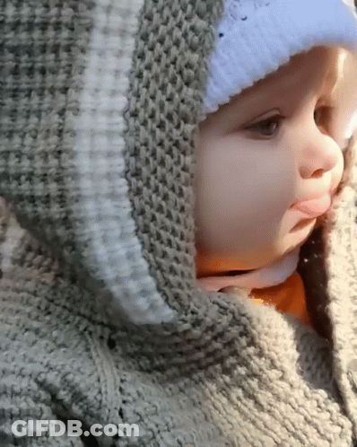 A Baby Wearing A Sweater With A Hood And A White Hat GIF