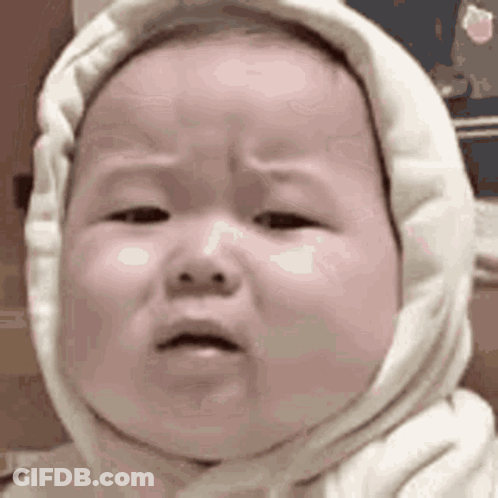 A Baby Wearing A White Hooded Sweater Is Crying . GIF