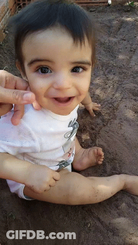A Baby Wearing A White Shirt With A Mouse On It Smiles For The Camera GIF