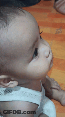 A Baby Wearing A White Tank Top Looks Up At Something GIF