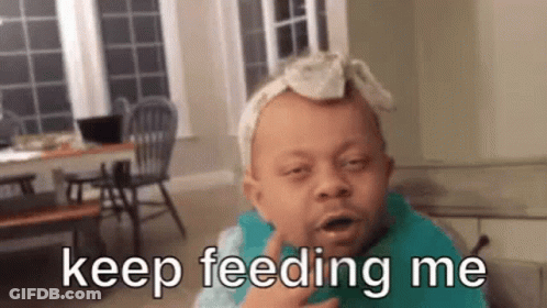 A Baby With A Bandana On His Head Is Wearing A Bib And Saying Keep Feeding Me . GIF