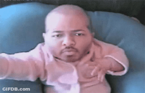 A Baby With A Beard Is Sitting On A Blue Pillow Looking At The Camera . GIF