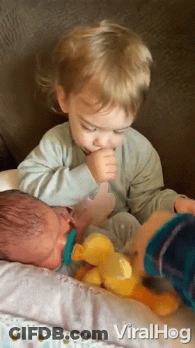 A Baby With A Pacifier In His Mouth Is Being Held By A Young Boy . GIF
