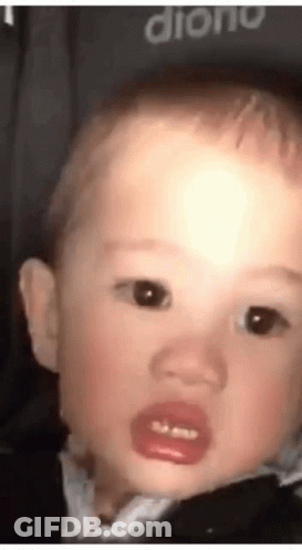 A Baby With A Pacifier In His Mouth Is Making A Funny Face And Looking At The Camera . GIF