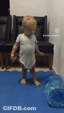 A Baby With A Pacifier In His Mouth Is Walking On A Blue Mat GIF