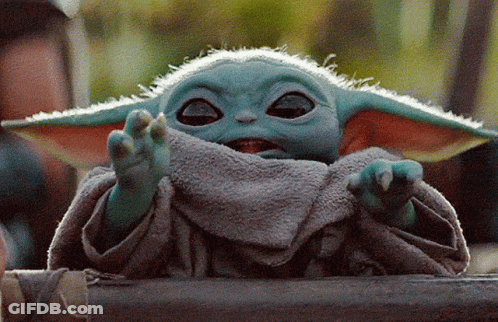 A Baby Yoda From The Mandalorian Is Sitting On A Wooden Fence . GIF