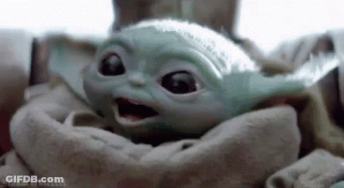 A Baby Yoda Is Sitting In A Blanket And Looking At The Camera . GIF