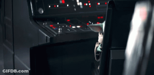 A Baby Yoda Is Sitting In A Chair In Front Of A Control Panel In A Dark Room . GIF