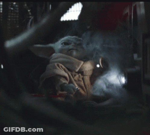 A Baby Yoda Is Sitting In A Dark Room With A Light Shining On It GIF