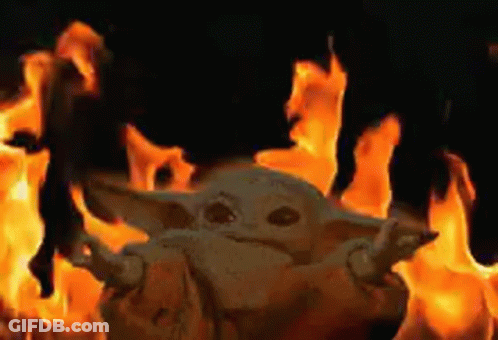 A Baby Yoda Is Standing In Front Of A Fire In A Dark Room . GIF