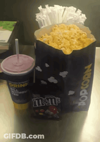 A Bag Of M & M 'S Sits Next To A Bag Of Popcorn On A Table GIF