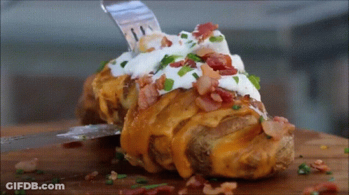A Baked Potato Covered In Cheese Bacon Sour Cream And Green Onions GIF