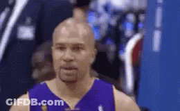A Bald Basketball Player Wearing A Purple Jersey Is Standing In Front Of A Blue Wall . GIF