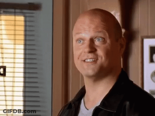 A Bald Man In A Black Jacket Looks At The Camera GIF