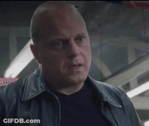 A Bald Man In A Black Jacket Looks Up At Something GIF