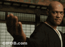 A Bald Man In A Black Robe Is Waving His Hand In Front Of A Window GIF