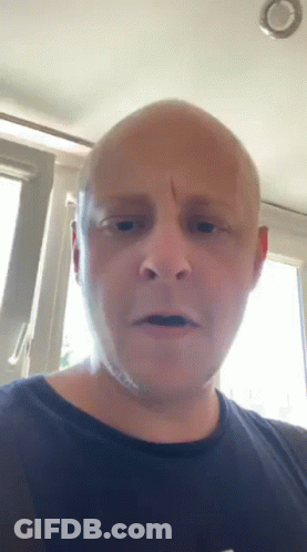 A Bald Man In A Black Shirt Is Looking At The Camera GIF