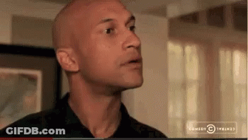 A Bald Man In A Black Shirt Is Standing In Front Of A Window In A Living Room . GIF