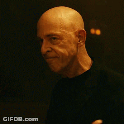 A Bald Man In A Black Shirt Is Waving His Hand In The Dark GIF