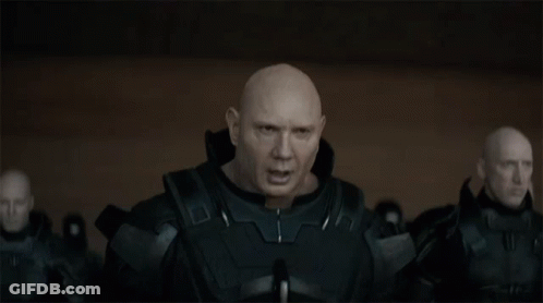 A Bald Man In A Black Suit Is Standing In Front Of A Group Of Bald Men GIF