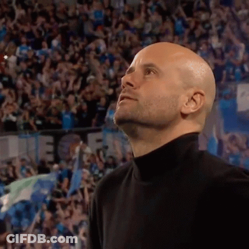 A Bald Man In A Black Turtleneck Stands In Front Of A Crowd And Looks Up GIF