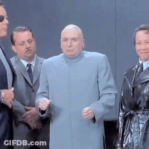 A Bald Man In A Blue Coat Is Standing In A Group Of People GIF