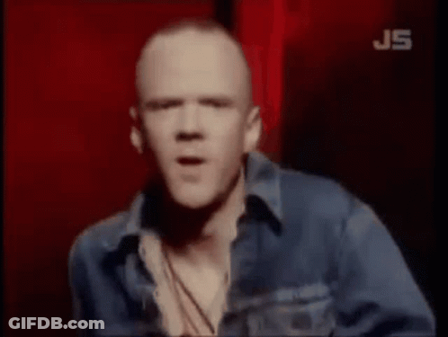 A Bald Man In A Blue Denim Jacket Is Standing In Front Of A Red Background . GIF
