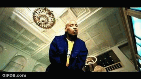 A Bald Man In A Blue Jacket Is Standing In A Room With A Chandelier . GIF