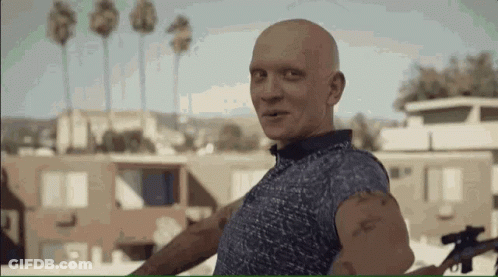 Bald Man In Blue Shirt Holding Gun Smiling GIF