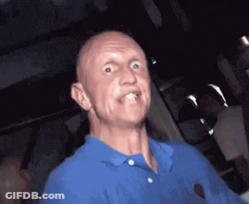 A Bald Man In A Blue Shirt Is Making A Funny Face . GIF