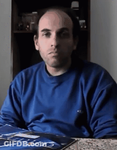A Bald Man In A Blue Shirt Is Sitting At A Table With A Magazine On It GIF
