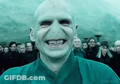 A Bald Man In A Blue Shirt Is Smiling In Front Of A Crowd Of People . GIF