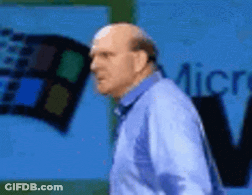 A Bald Man In A Blue Shirt Is Standing In Front Of A Microsoft Sign . GIF