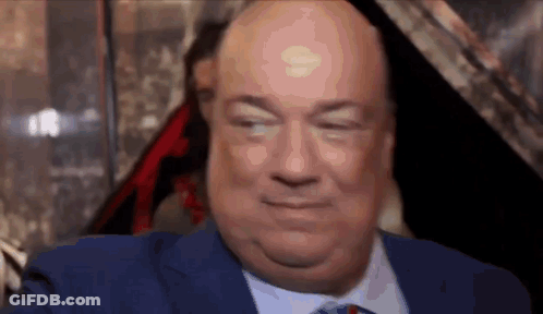 A Bald Man In A Blue Suit And Tie Is Smiling . GIF